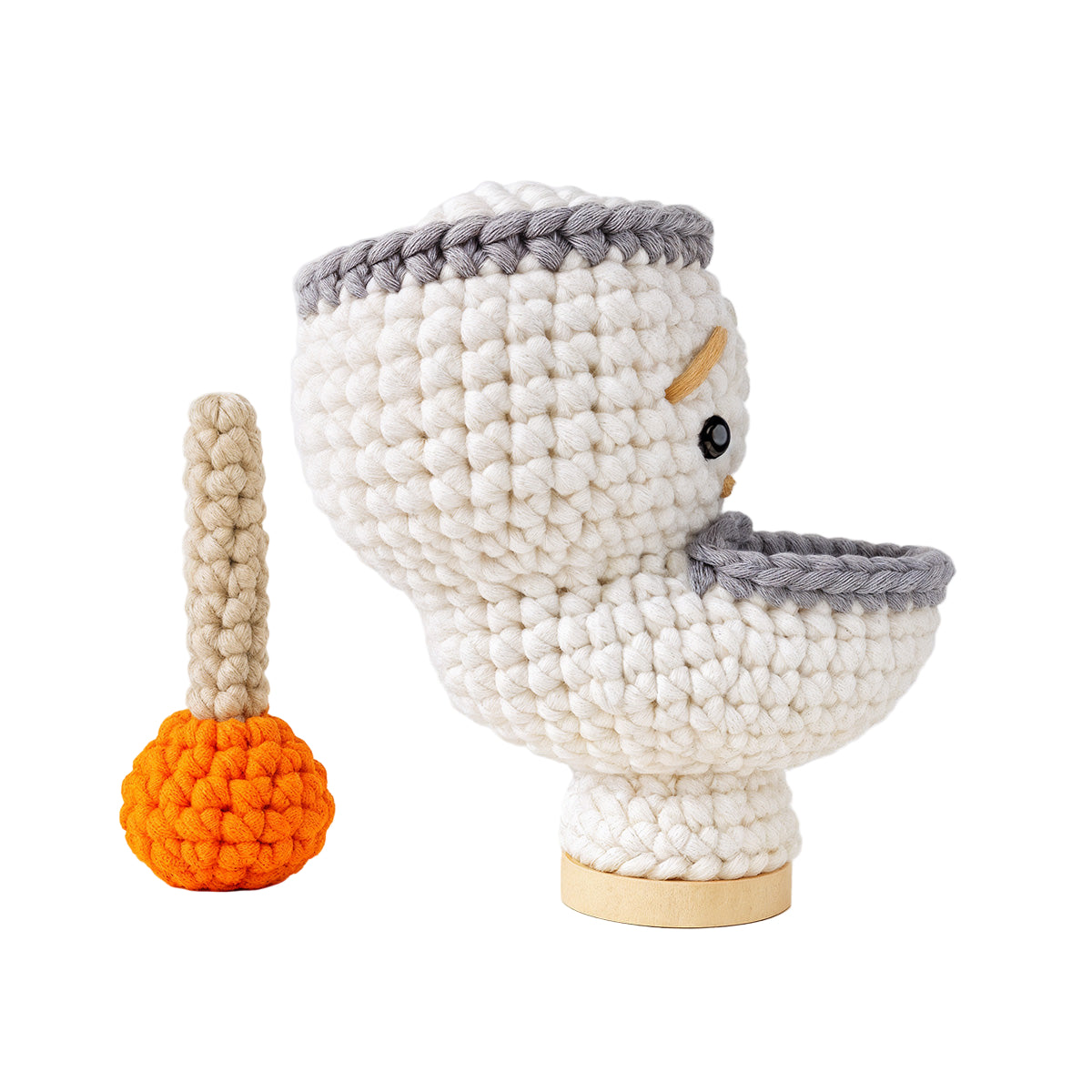 Splashy The Toilet Crochet Pattern features a white crocheted toilet with a gray rim and an orange-beige plunger—an amusing crochet amigurumi gift, ideal for quirky decor lovers or unique collection additions.