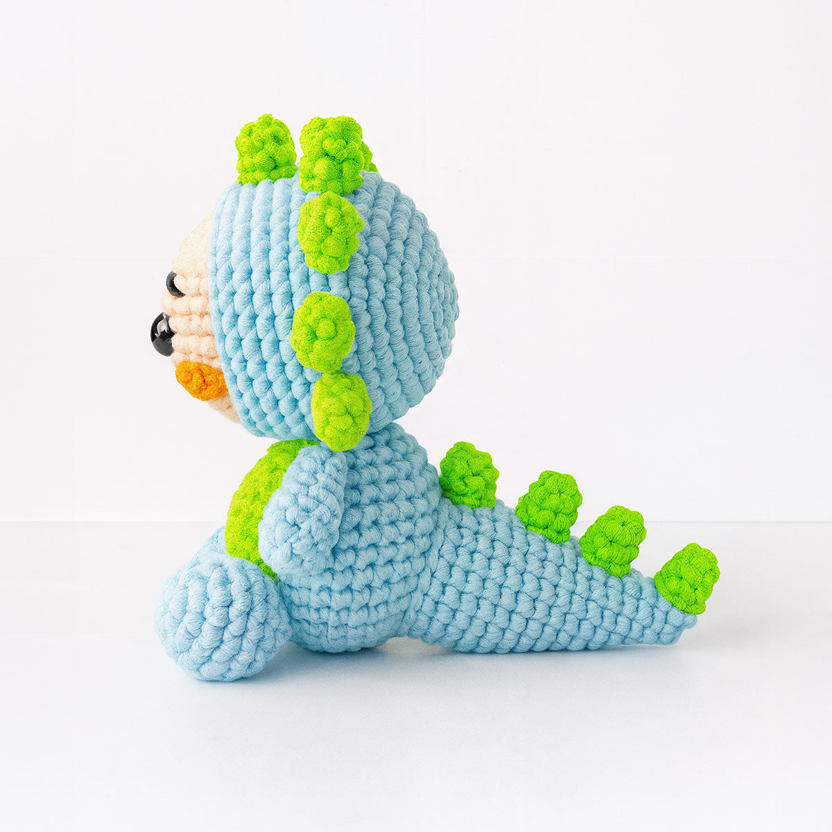 Spiky The Dino is a crocheted plush toy dinosaur with a blue body and bright green accents, crafted using an advanced crochet pattern and pictured in profile against a plain white background.