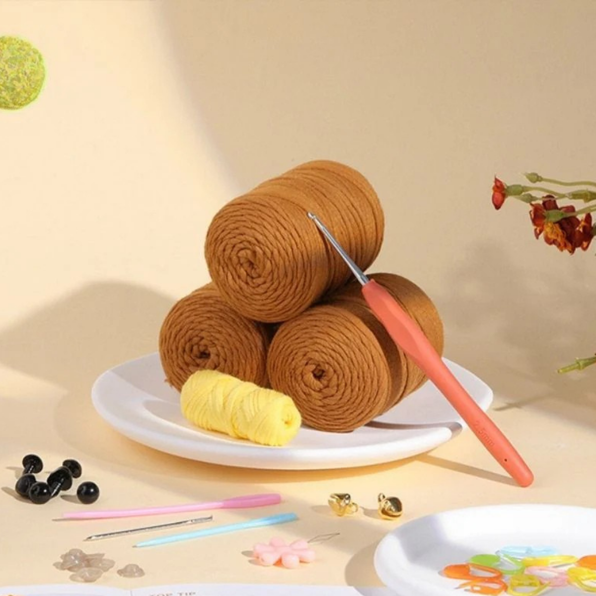 Three brown yarn skeins, a crochet hook, yellow thread, beads, and more—everything you need in the Crochet Poodle Kit to assemble your own poodle or start a fun beginner crochet project.