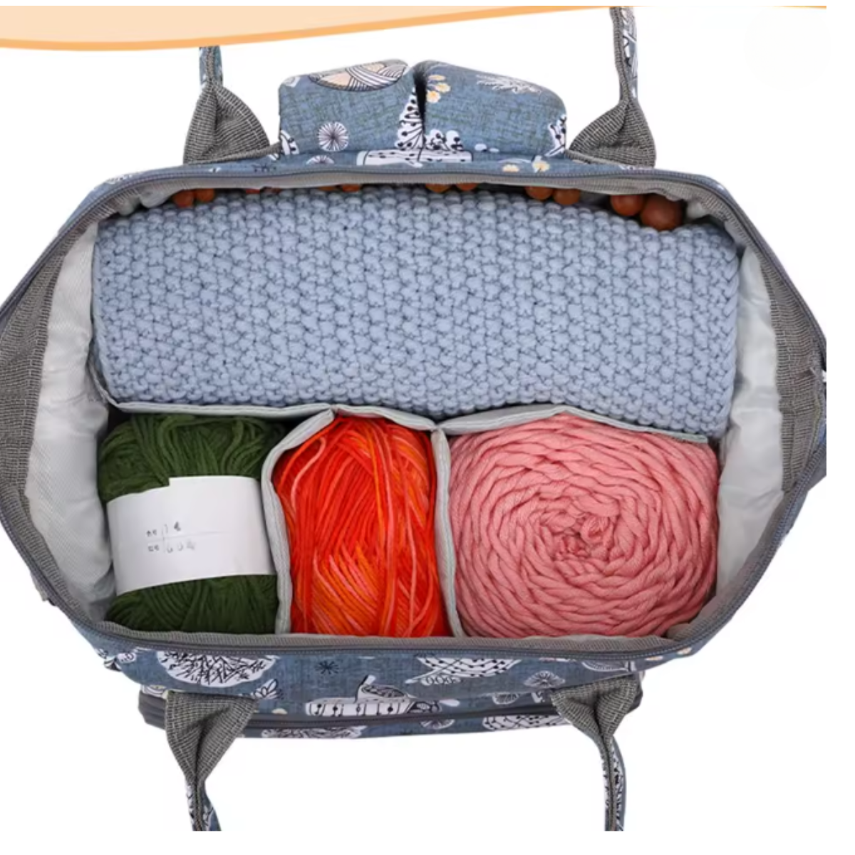Oxford Serenity Luxe Bag - Yarn Organizer shown open with a blue crochet project on top and green, orange, and pink yarn skeins neatly arranged below inside its floral-patterned design.