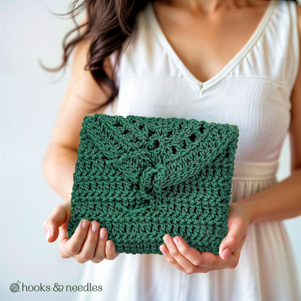A woman in a white dress holds the Petite Purse Crochet Pattern—a green, hand-crocheted purse with a flap closure. This elegant accessory features a beginner-friendly crochet design.