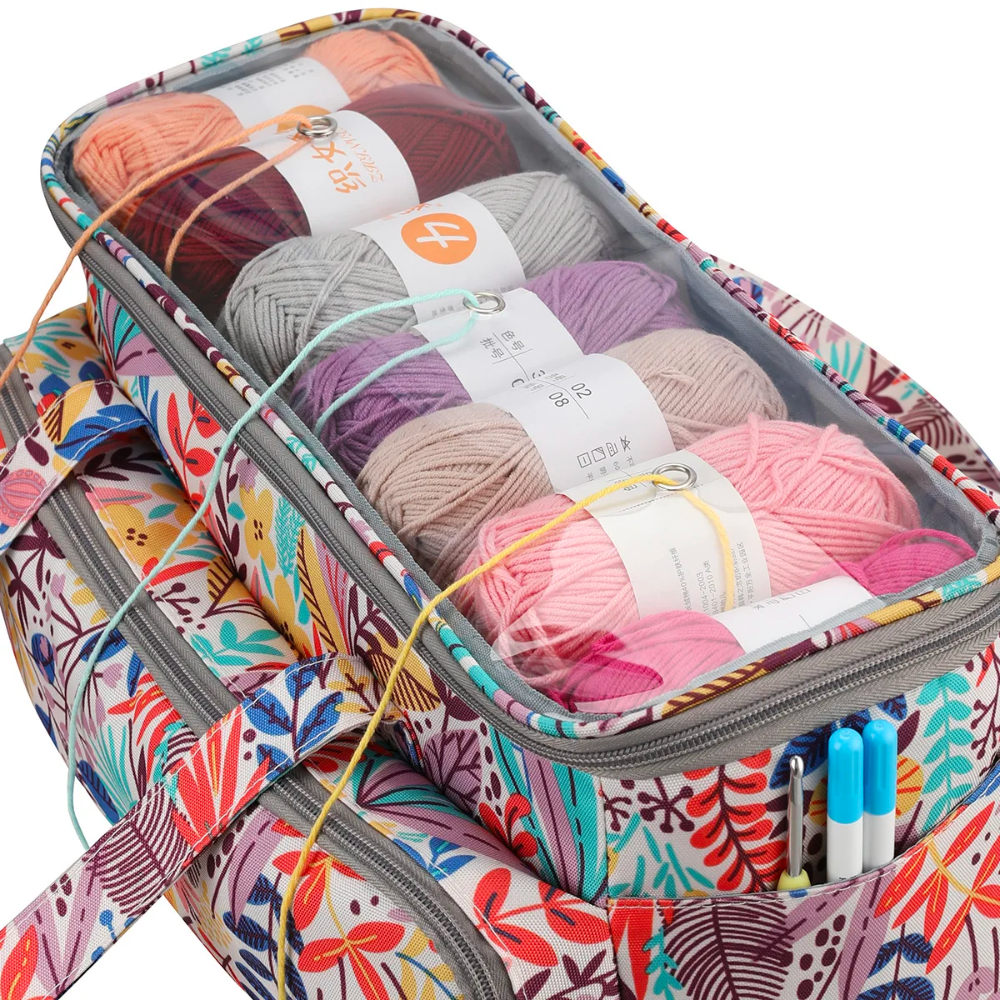 The Crochet Knitting Bag Organizer (Bundle8) holds colorful yarn balls inside its floral-patterned design, with its partially open transparent top revealing pink, gray, purple, and orange shades. Pens are neatly stored in a front pocket of this versatile knitting accessory.