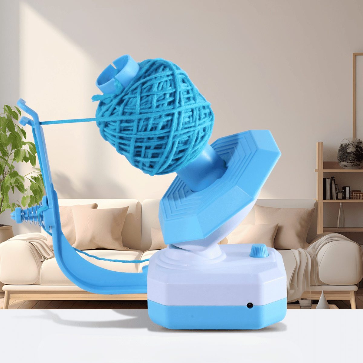 An Electric Yarn Winder with blue yarn is placed on a table in a modern living room, featuring a sofa and a plant in the background.