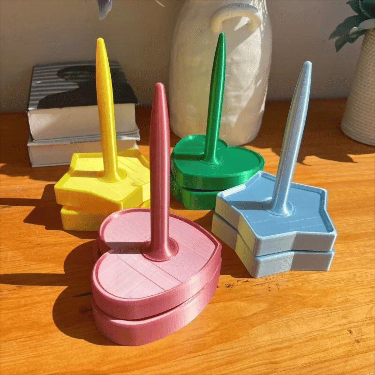 A Spinning Yarn Holder is displayed on a wooden surface with books and a white vase in the background.