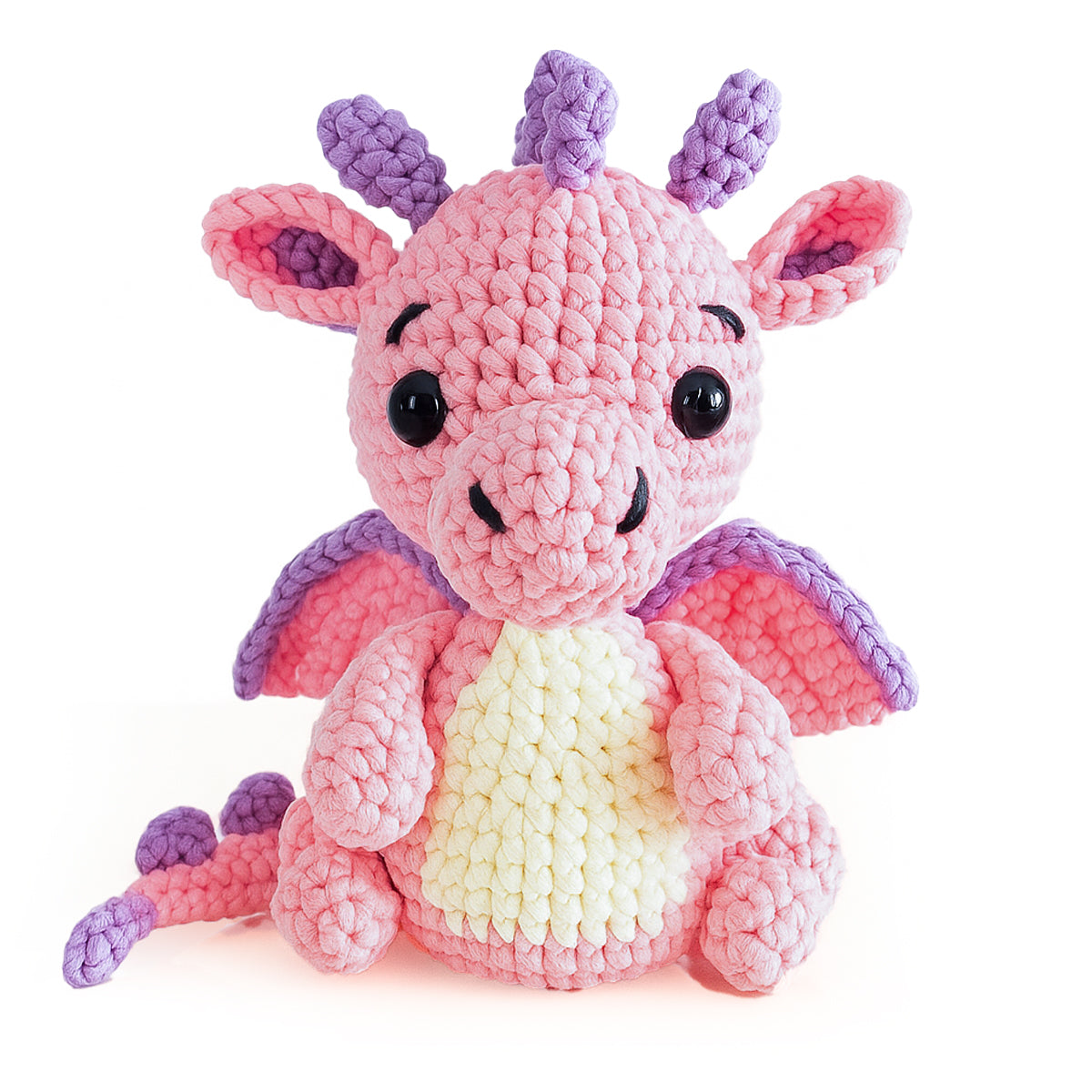 Sparkle The Dragon Crochet Pattern features a plush amigurumi dragon with pink and purple scales, large black eyes, purple wings, and a cream belly—an ideal choice for your next intermediate crochet project.