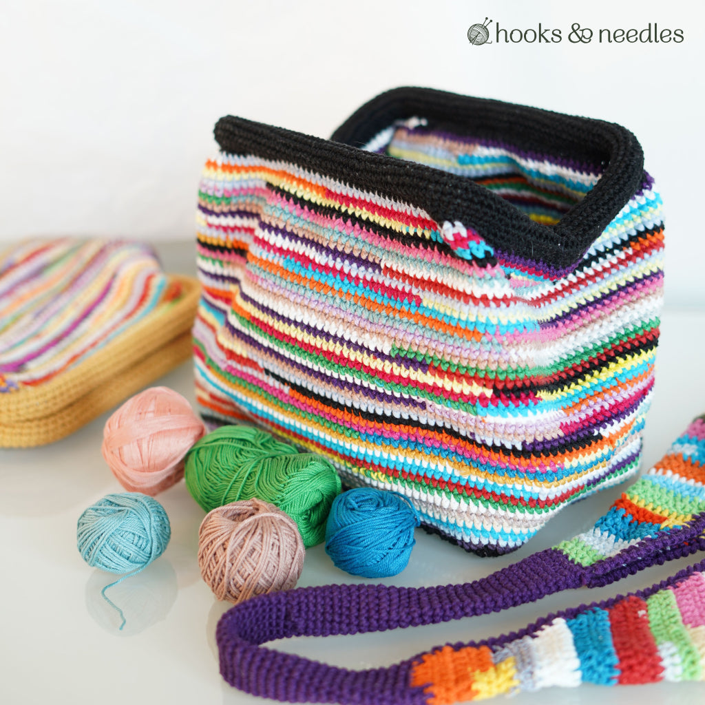 The Upcycled Color Clutch Crochet Pattern features a vibrant striped design, shown with yarn scraps and a coordinating crocheted strap.