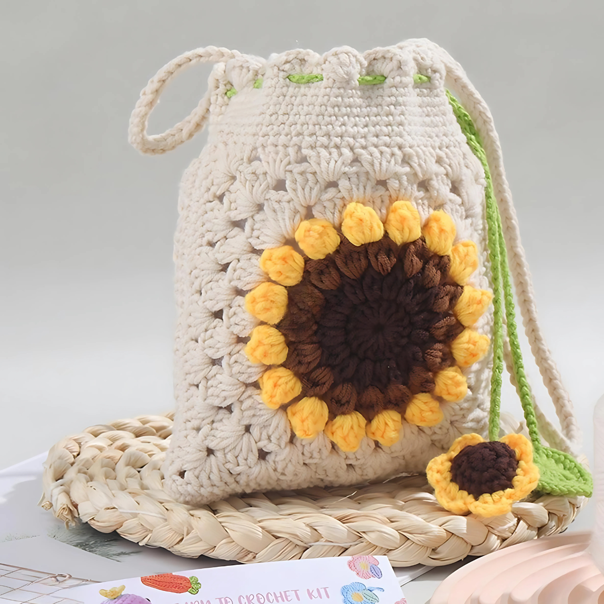 The Sunflower Crochet Bag Kit lets you create a handmade drawstring bag with a sunflower design and matching charm on a green string—perfect for fans of floral accessories or anyone wanting to try crochet.