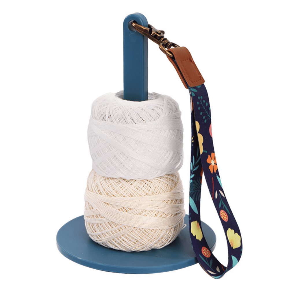 The Wrist Yarn Holder comes with two spools of white and cream thread and a floral strap attached to the top hook, making it ideal for travel crafting and hands-free yarn control.