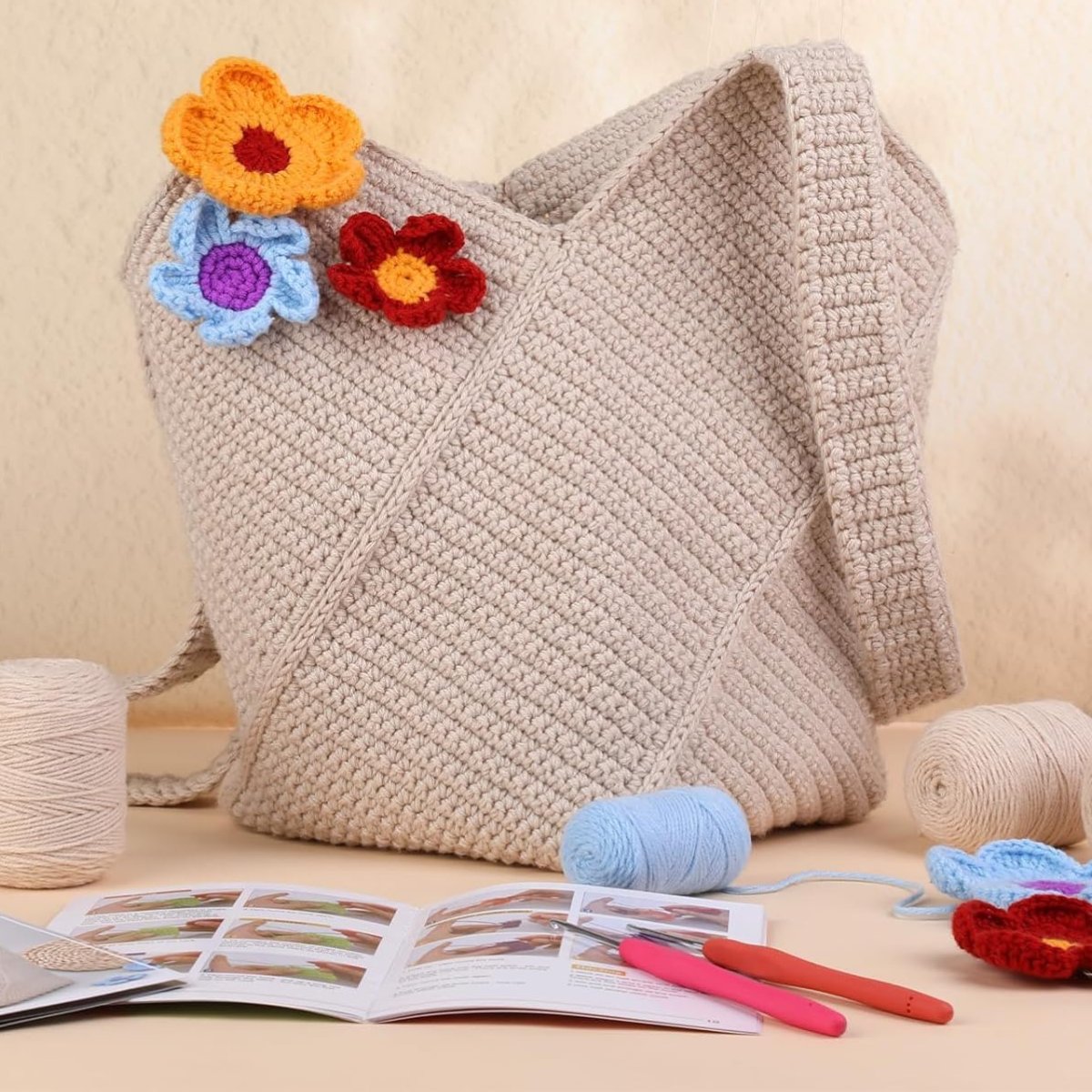 The Bohemian Crochet Tote Bag Kit includes beige cotton yarn and colorful crocheted flowers, plus all essentials—yarn balls, hooks, and an instruction booklet—making it perfect for crafting a unique bag on any surface.