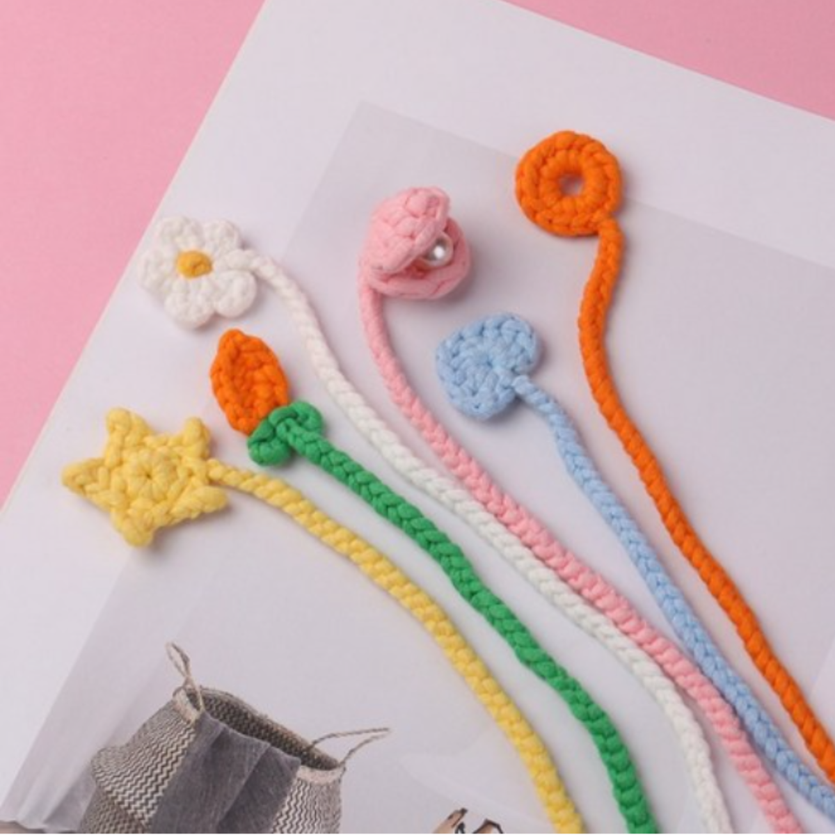 Five adorable animal crochet bookmarks from the Cute Animal Crochet Bookmark Kit are displayed on an open book with a pink background, perfect for expanding your collection or adding to any DIY crochet project.