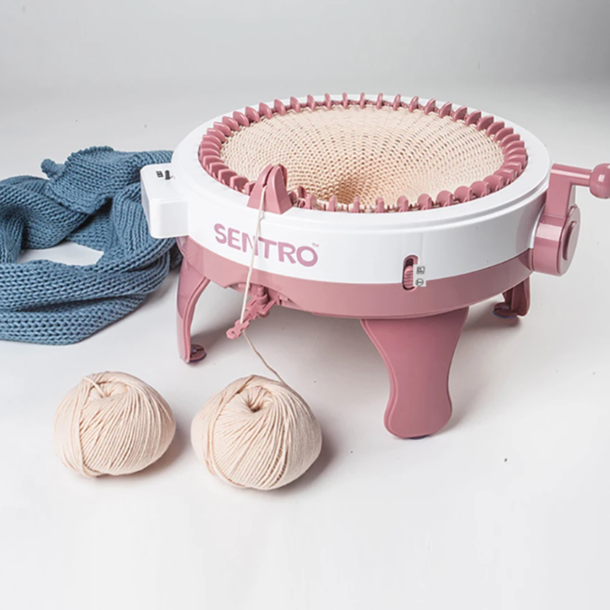 A pink and white 48 Needles Knitting Machine with Row Counter, shown with two beige yarn balls and blue knitted fabric on a white surface, ideal for fast knitting projects.