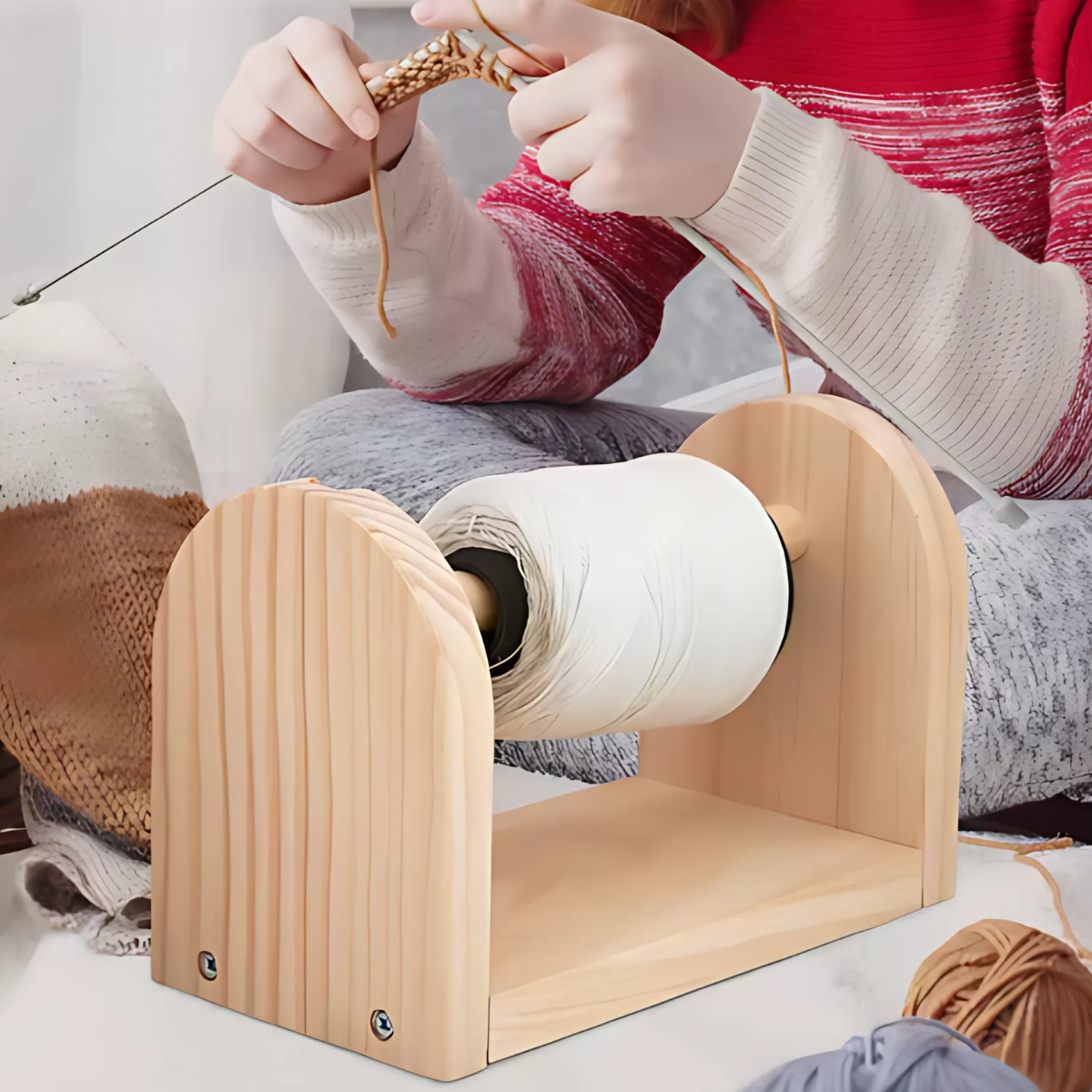 A person knits with tan yarn while the Wooden Yarn Dispenser smoothly holds a spool of white yarn in the foreground, keeping it steady for an easier and more enjoyable crafting experience.