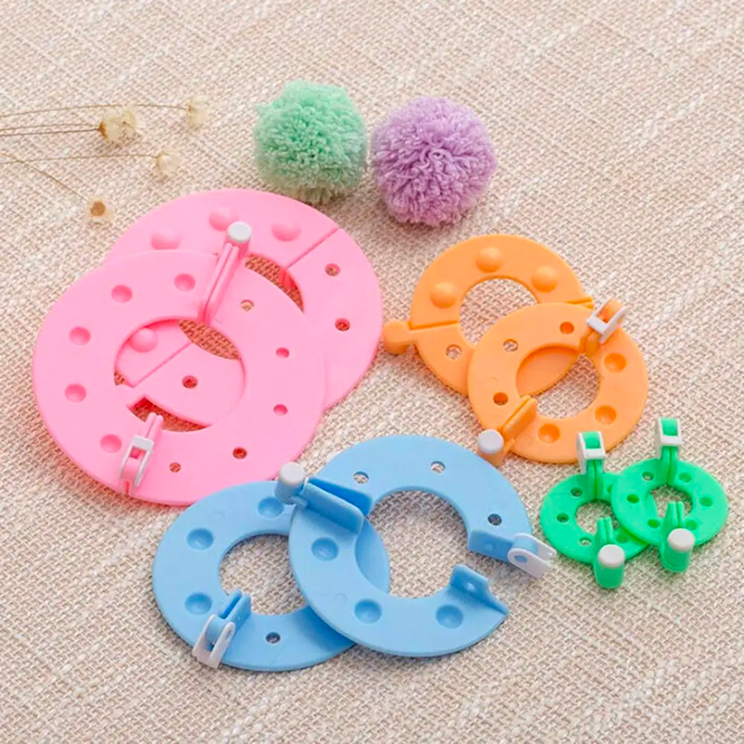 The Pom Pom Maker Set, composed of vibrant and durable materials, is neatly arranged in various sizes on a fabric surface. Two fluffy pom-poms sit nearby, ready to inspire your next crafting project.