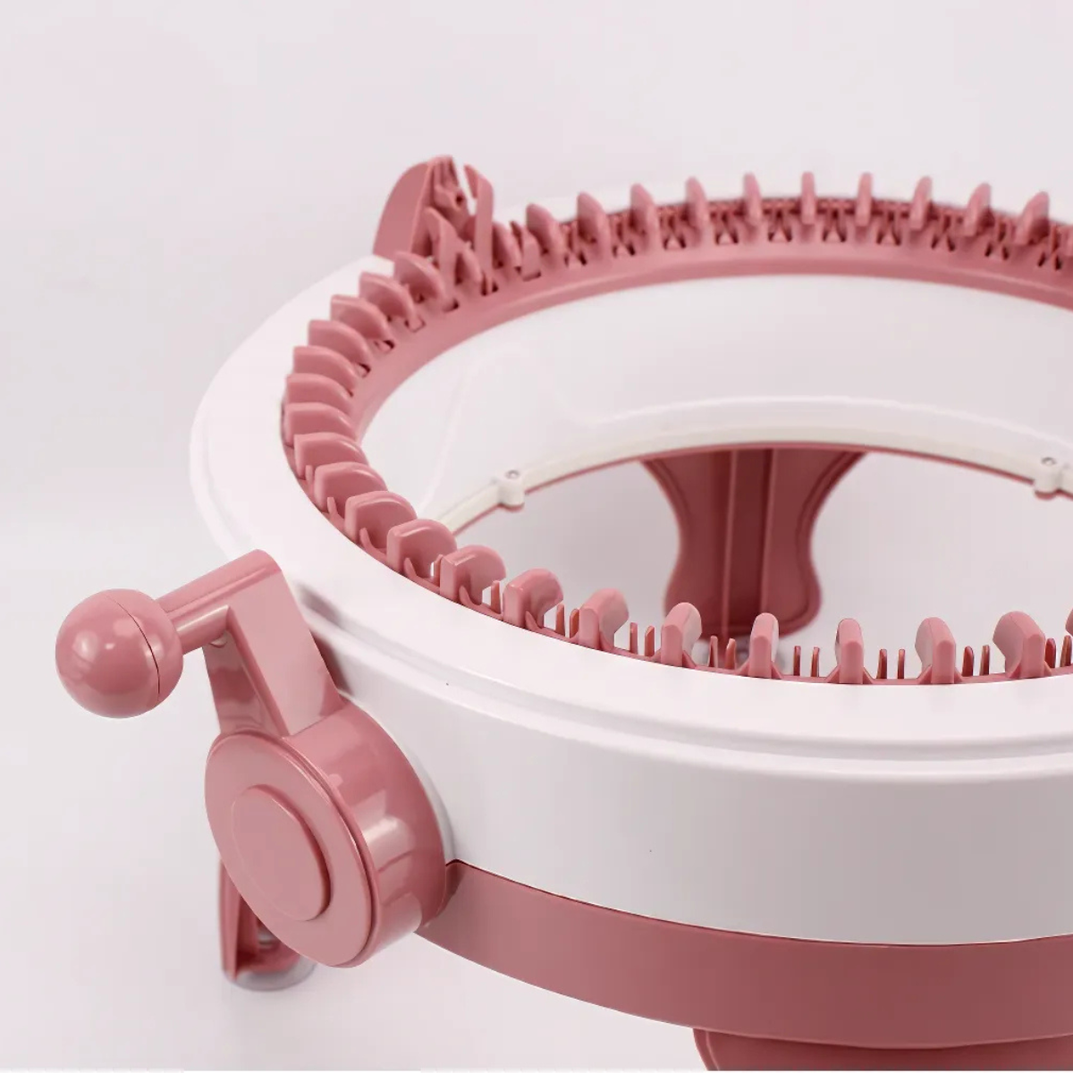 A close-up view of the 48 Needles Knitting Machine with Row Counter in pink and white, featuring a hand crank, evenly spaced plastic needles, and an integrated row counter for fast knitting.