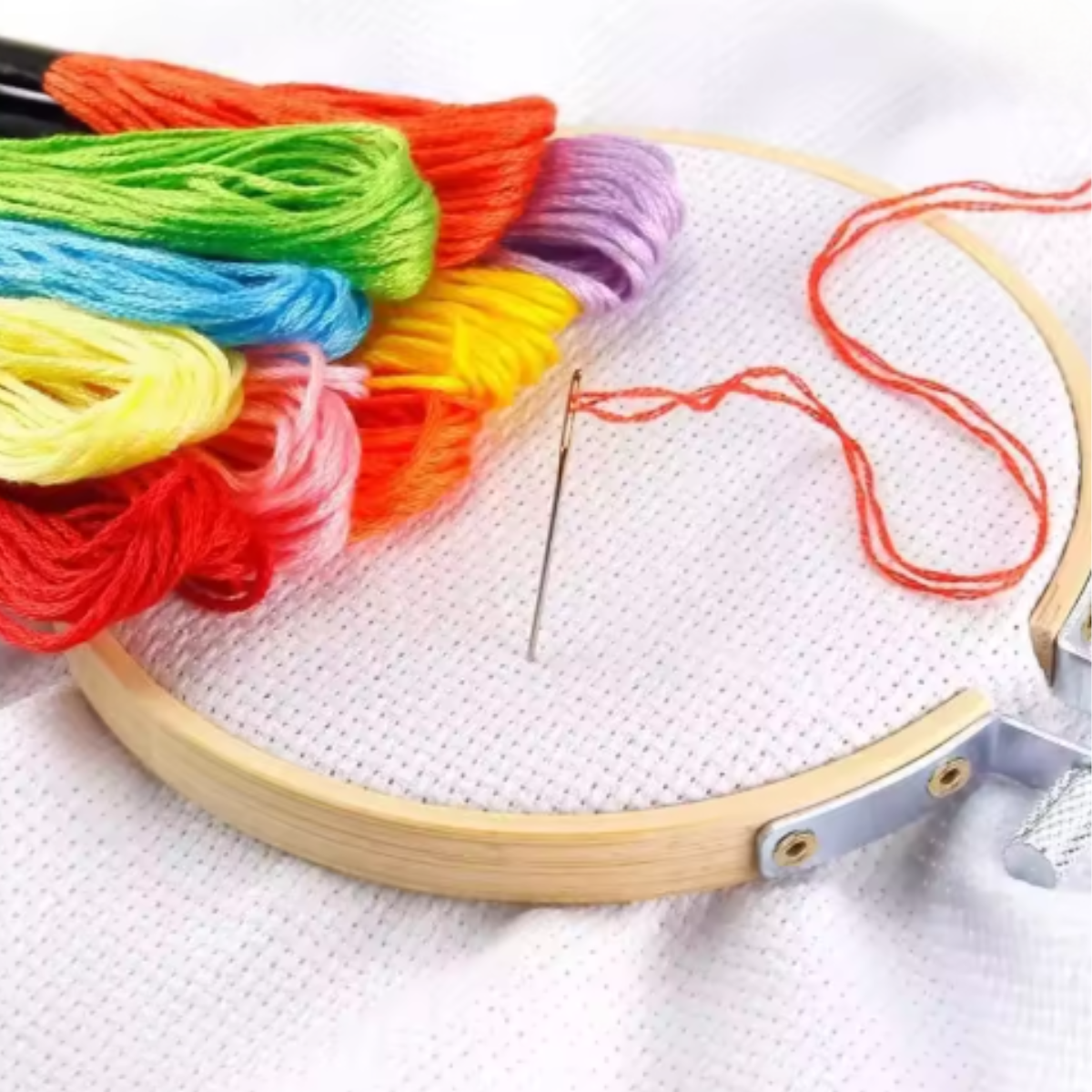 The Embroidery Floss Set includes an embroidery hoop with white fabric, a threaded needle, and several colorful floss skeins—perfect essentials for detailed cotton thread work.