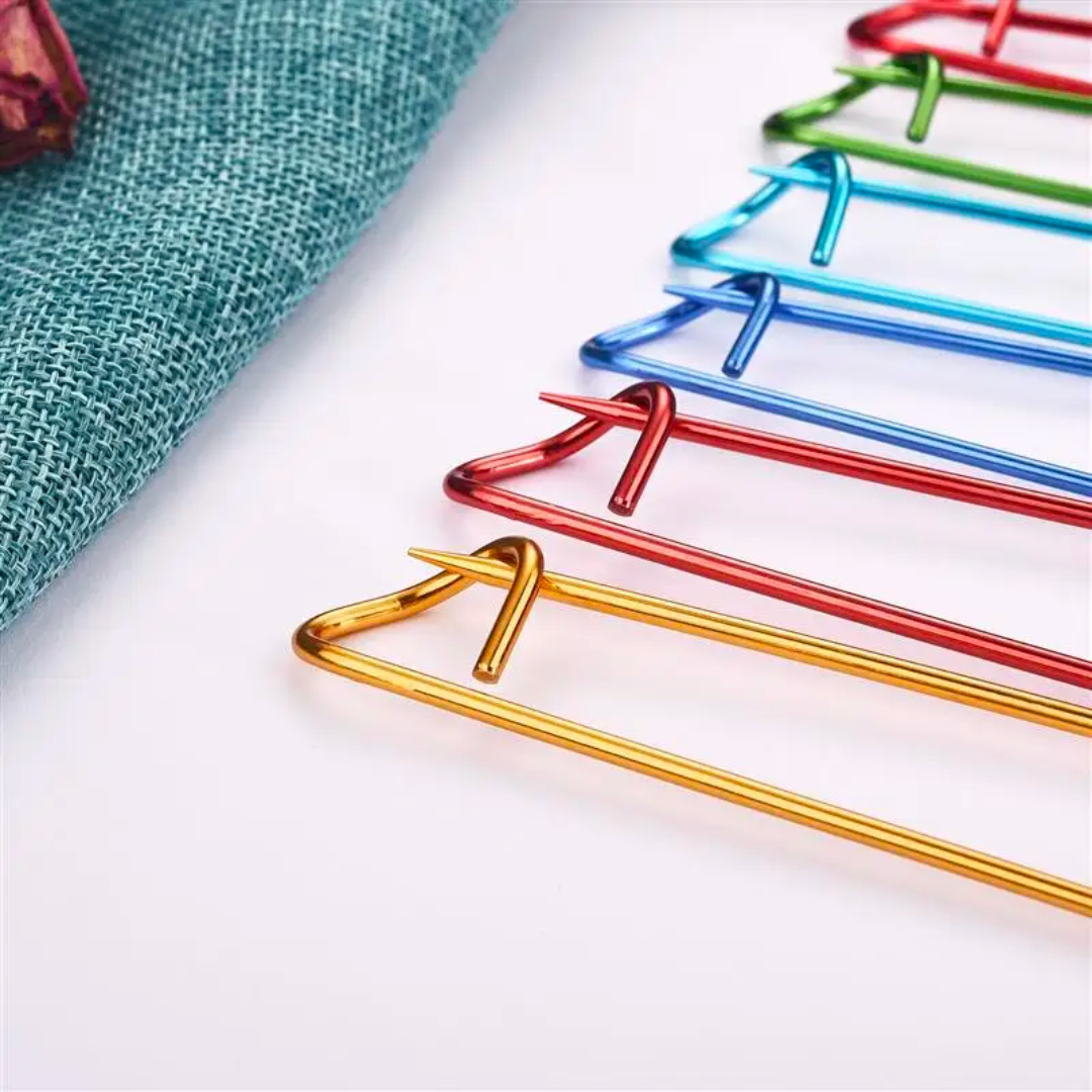 Close-up of colorful metal hangers, reminiscent of the Stitch Holder Set 6pcs, arranged in a row on a light surface next to a teal fabric.