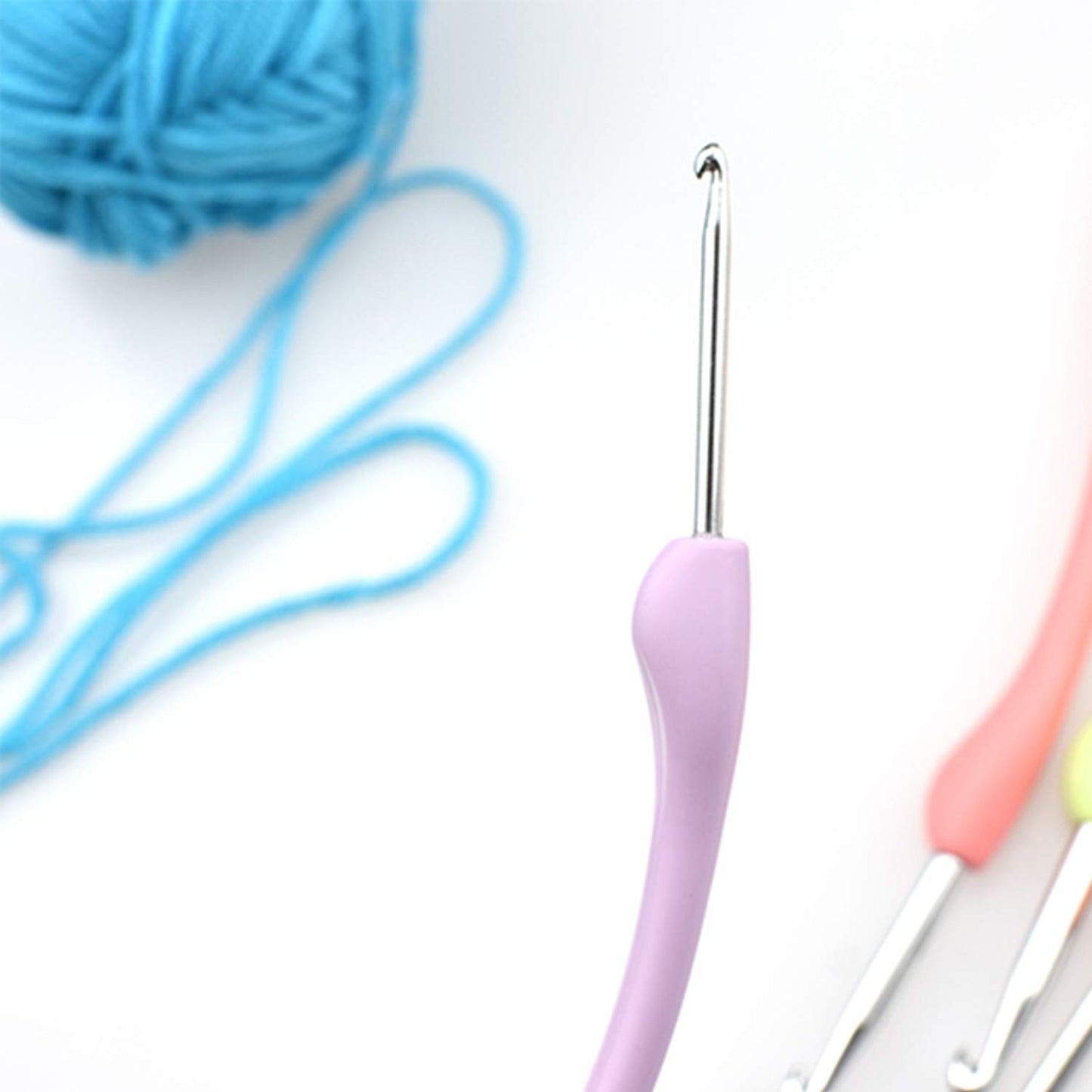 A close-up of a purple-handled hook from the Vintage-Style Crochet Hook Set 8 Pcs with Soft Handle, shown with a ball of blue yarn and two other crochet hooks in the background.