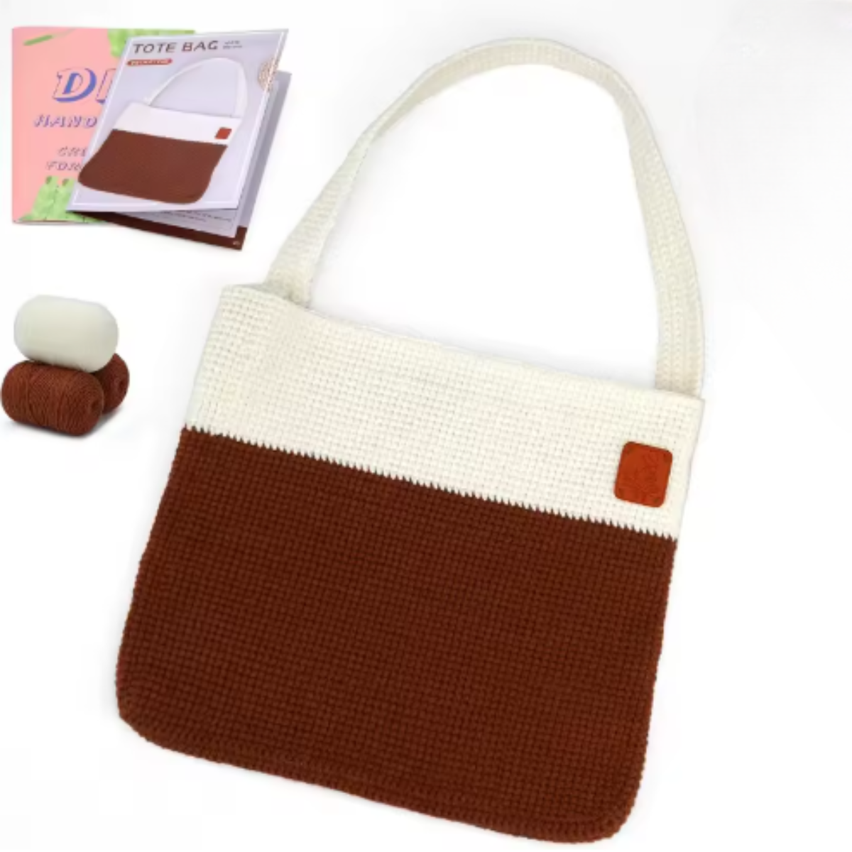 The Modern Crochet Tote Bag Kit includes two balls of cotton yarn, an instruction booklet, and materials to make a stylish two-tone tote with a cream upper section, brown lower section, and a small brown patch.