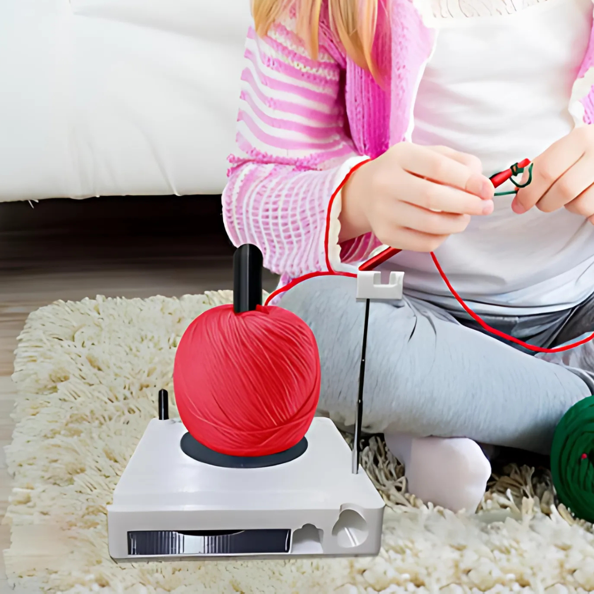 A child sits on a rug using a Spinning Yarn Holder with Tool Storage, holding knitting needles while red yarn flows smoothly.