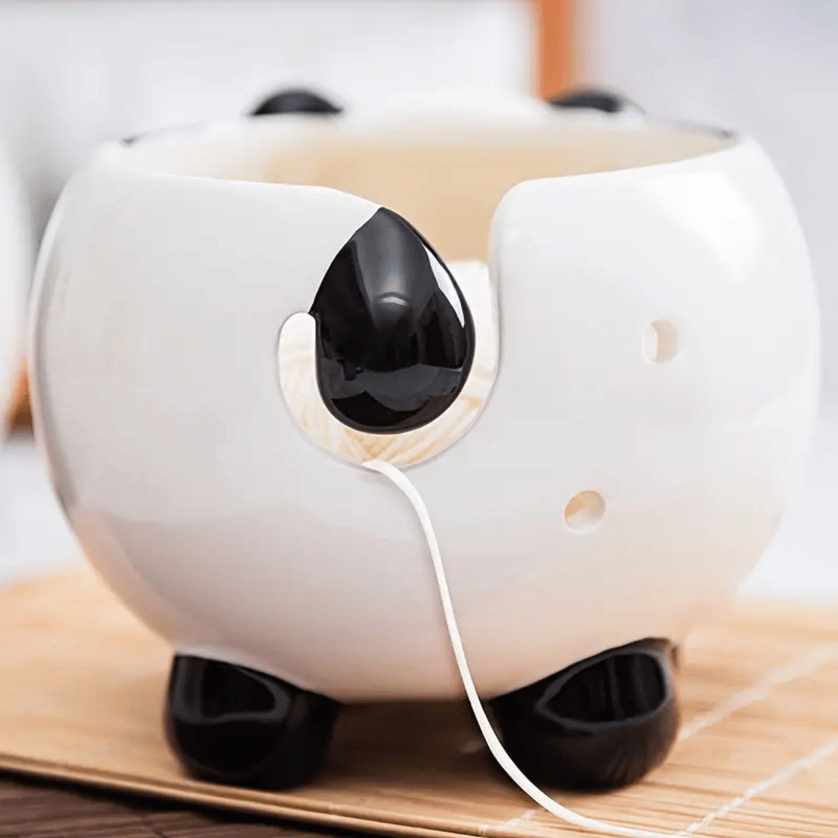 The Panda Ceramic Yarn Bowl—round and panda-shaped with black ears, feet, and tail—holds a white spoon in its side slot, making it a charming way to serve snacks during beginner-friendly knitting loom sessions.