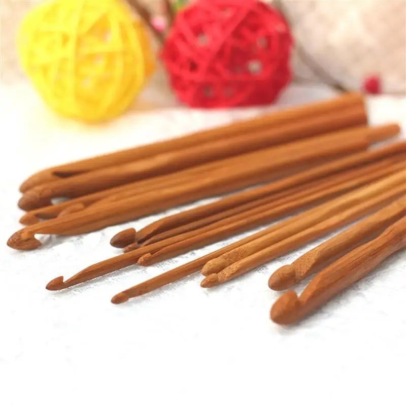 A set of Bamboo Crochet Hooks 12 Pcs is elegantly arranged on a white surface, complemented by red and yellow decorative balls in the background, ideal for individuals who value sustainable crafting tools.