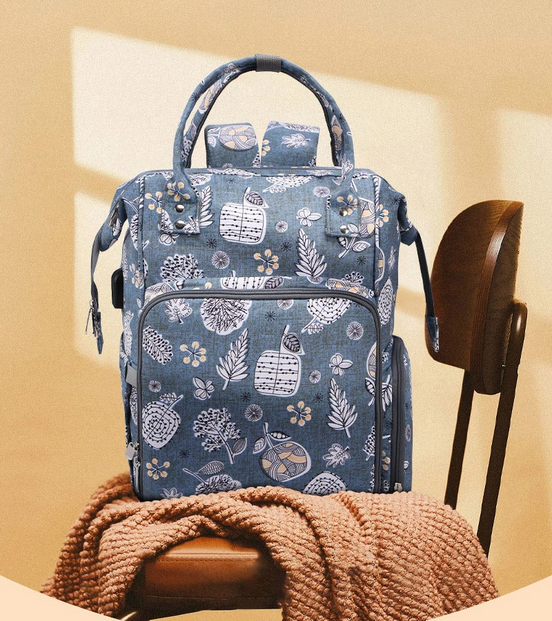 An Oxford Serenity Luxe yarn organizer bag in a blue floral pattern, part of the bundle, rests on a wooden chair covered with a textured brown blanket, providing an elegant solution for storing your knitting and crocheting essentials.