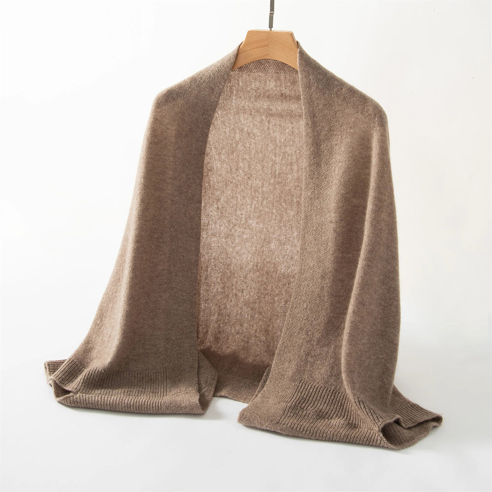 A Cashmere Knitted Poncho Scarf (bundle), exuding luxurious comfort, is hanging on a wooden hanger against a plain background.