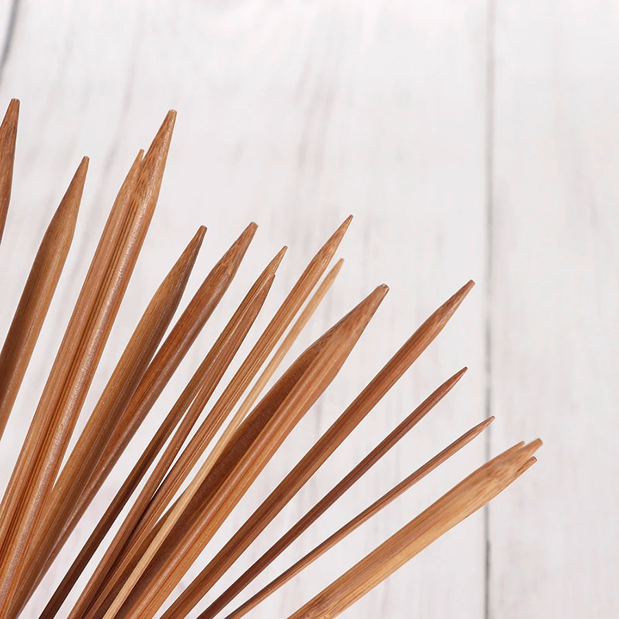 Close-up of the pointed ends of several knitting needles from the 36 Pcs Bamboo Knitting Needles set, showcasing their smooth finish as they fan out against a light wood background.