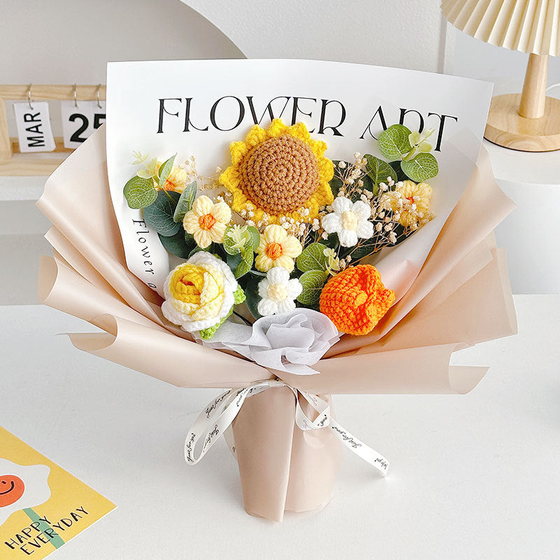 A unique bouquet featuring a Crochet Sunflower Bouquet: Blooms That Never Wilt, adorned with white daisies and orange blossoms. It's elegantly wrapped in beige paper and tied with a white ribbon, reflecting timeless beauty. Tucked at the top is a card labeled "Flower Art.