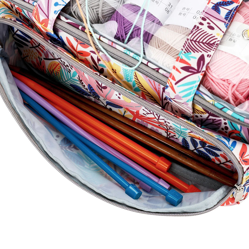 The Knitting Bag: Yarn Organizer, adorned with vibrant floral patterns, sits open to reveal an assortment of knitting accessories, including needles and various yarn skeins inside.