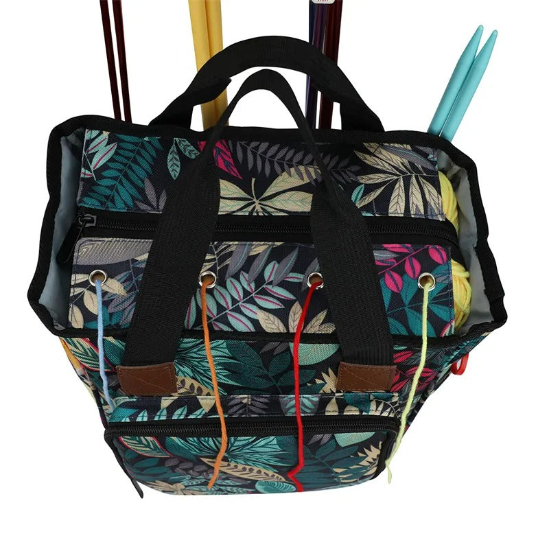 The Yarn Organizer Tote is a vibrant bag with a leaf pattern and black straps, ideal for craft enthusiasts, complete with knitting needles peeking out.