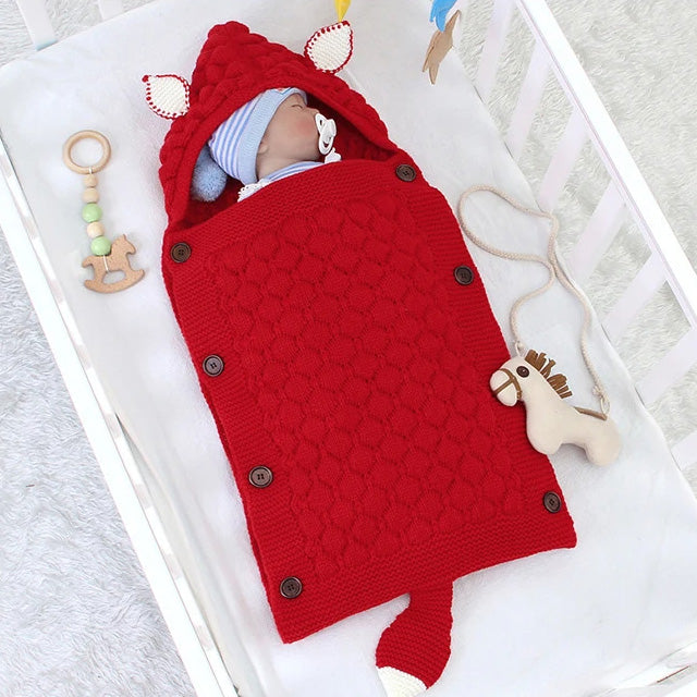 A baby sleeps in a crib, wrapped in a Knitted Baby Sleeping Bag Wrap Blanket. Nearby, a wooden toy and pacifier add to the adorable design of this soothing scene.