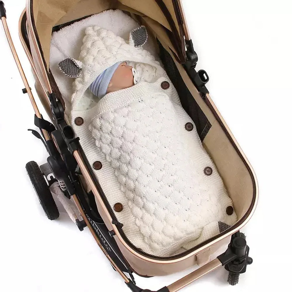 An adorable design combines with cozy comfort as a baby is nestled in a stroller, wrapped in the Knitted Baby Sleeping Bag Wrap Blanket (bundle) featuring a white, textured design with small ears.