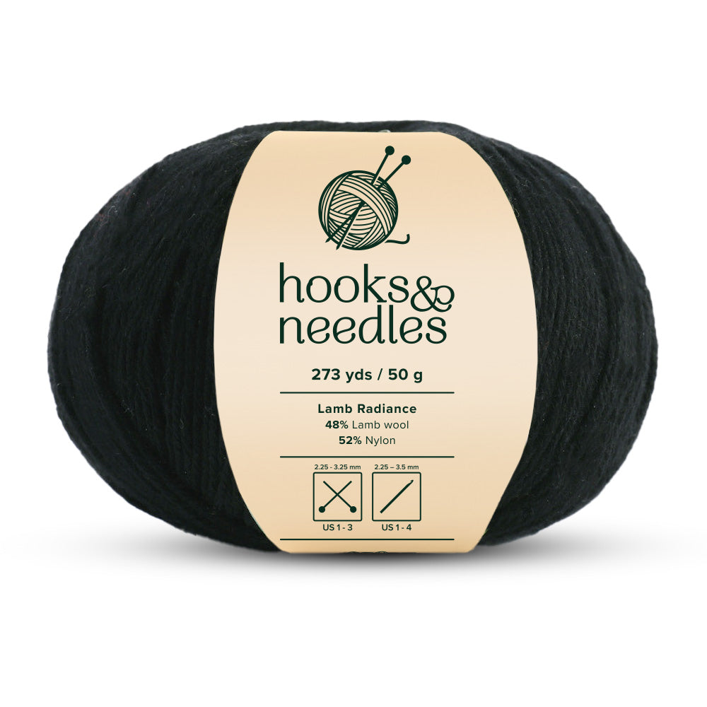 A ball of black Lamb Radiance Yarn 50g with a label that states "hooks & needles, super fine-weight yarn, 48% lamb wool, 52% nylon, 273 yds / 50 g." The label also displays the recommended knitting needle sizes.