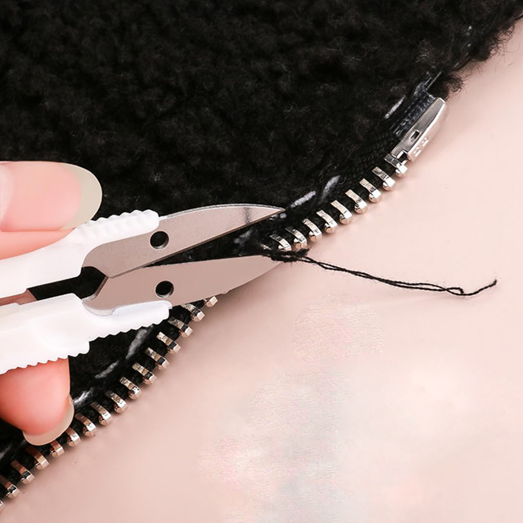 A hand uses white thread snips to trim a loose black thread near the zipper of a black item, ideal for finishing projects from the 29-Piece Crocheting Kit: Perfect for Beginners.