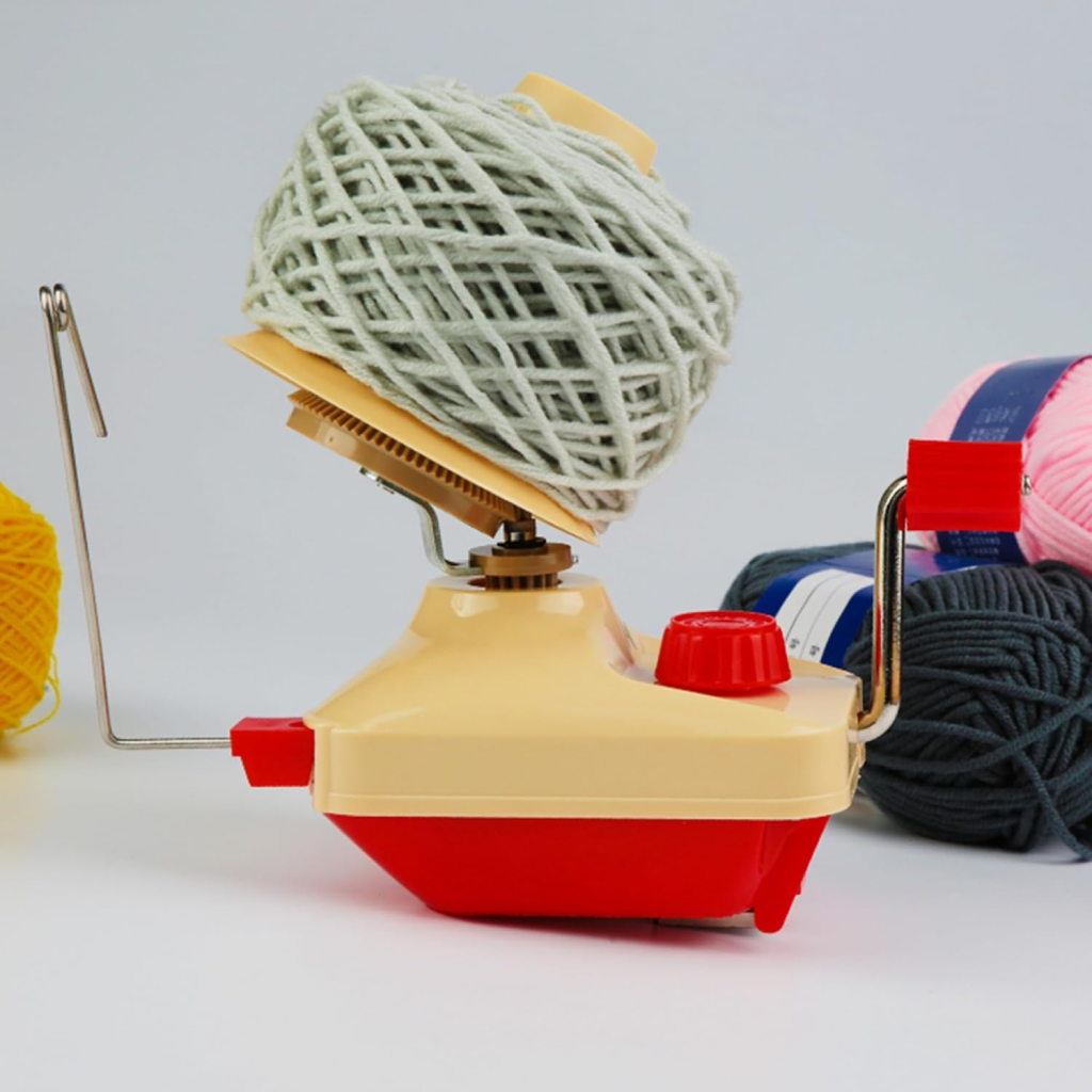 The Yarn Ball Winder, shown with a light gray yarn ball on top and colorful yarn balls around it, is perfect for crocheters and knitters. Set against a plain background.