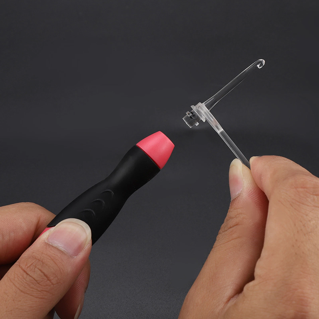 A hand holds the LED Crochet Hooks: 11-in-1 Rechargeable, featuring interchangeable black and pink handles, while another hand shows a clear plastic hook against a plain dark background.