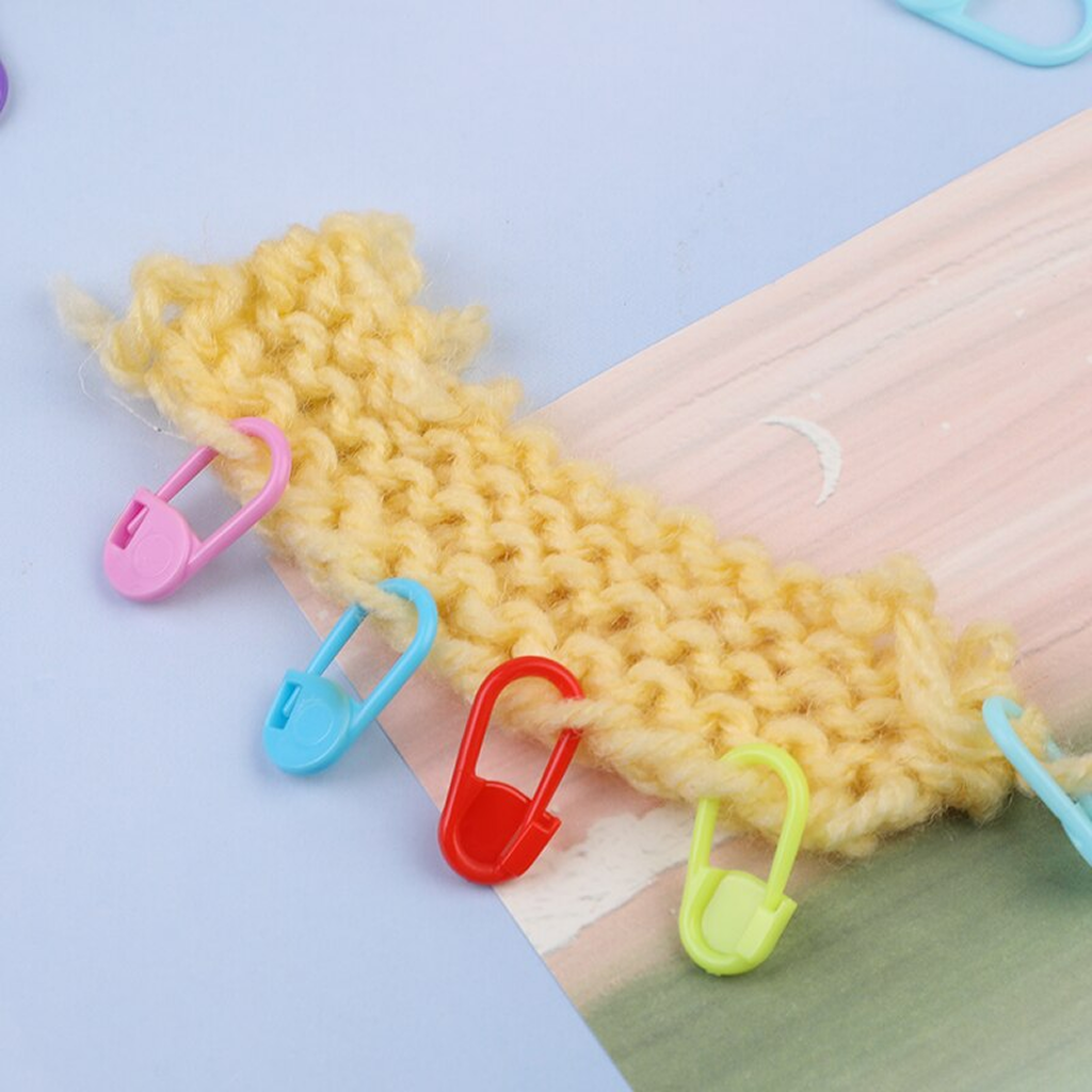 A yellow knitted swatch for yarn crafts is secured with Colorful Plastic Stitch Markers, displayed on a pastel background.