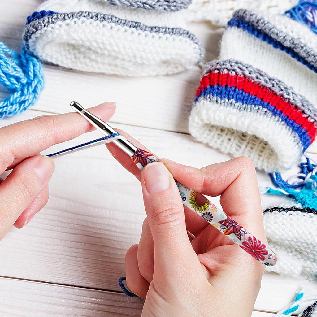 Using the 29-Piece Crocheting Kit: Perfect for Beginners, someone crochets with a comfortable hook and blue yarn, while finished pieces in white, gray, red, and blue are displayed on a wooden surface in the background.