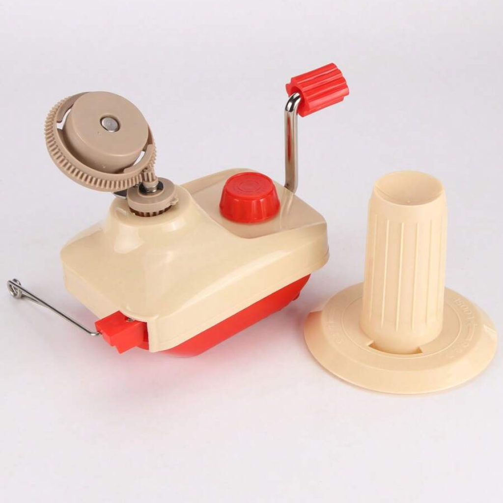 The Yarn Ball Winder features a beige and red plastic body, crank handle, and a separate beige cone holder—ideal for organizing yarn skeins for knitting or crocheting. Shown placed on a white surface.