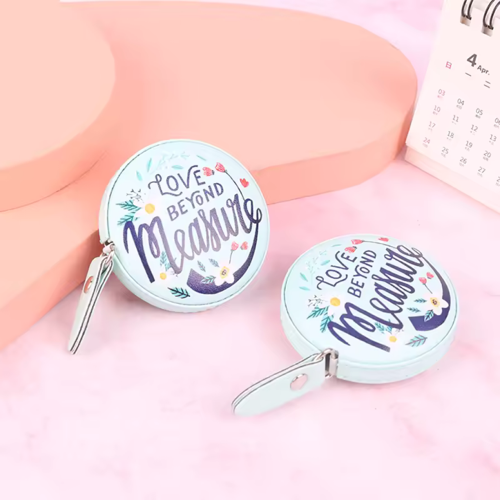 Two round tape measures with "Love Beyond Measure" sit on a pink surface by an April calendar, making them a thoughtful extra for the 29-Piece Crocheting Kit: Perfect for Beginners.