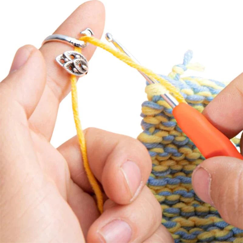 Hands crocheting with multicolored yarn using an orange-handled crochet hook and the Yarn Tension Control Ring, which embodies a creative spirit and is adorned with a flower design.