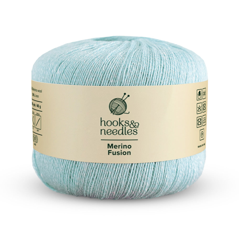 A 40g ball of light blue Merino Fusion Yarn with a lace-weight feel, featuring a "hooks & needles" label along with care symbols.