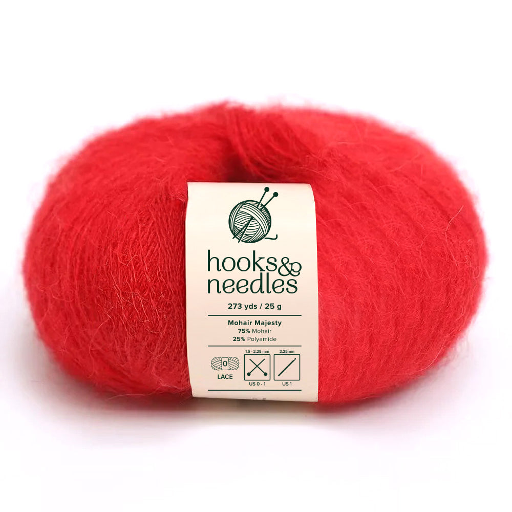 A skein of Mohair Majesty Yarn 25g in red provides a luxurious texture, composed of 75% mohair and 25% polyamide. This lace-weight yarn offers an impressive 273 yards per 25 grams and is showcased elegantly on a white background under the "hooks & needles" brand.
