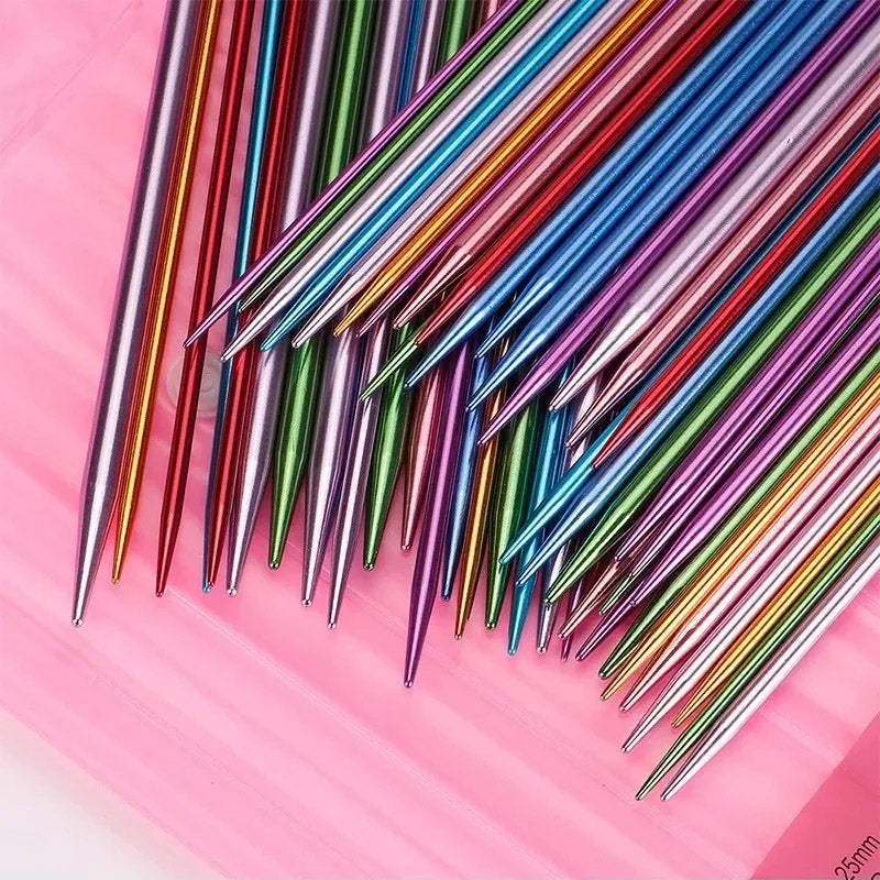 A vibrant array of the 55 Pcs Double Pointed Knitting Needle Set, featuring colorful aluminum needles, is spread out on a pink surface.
