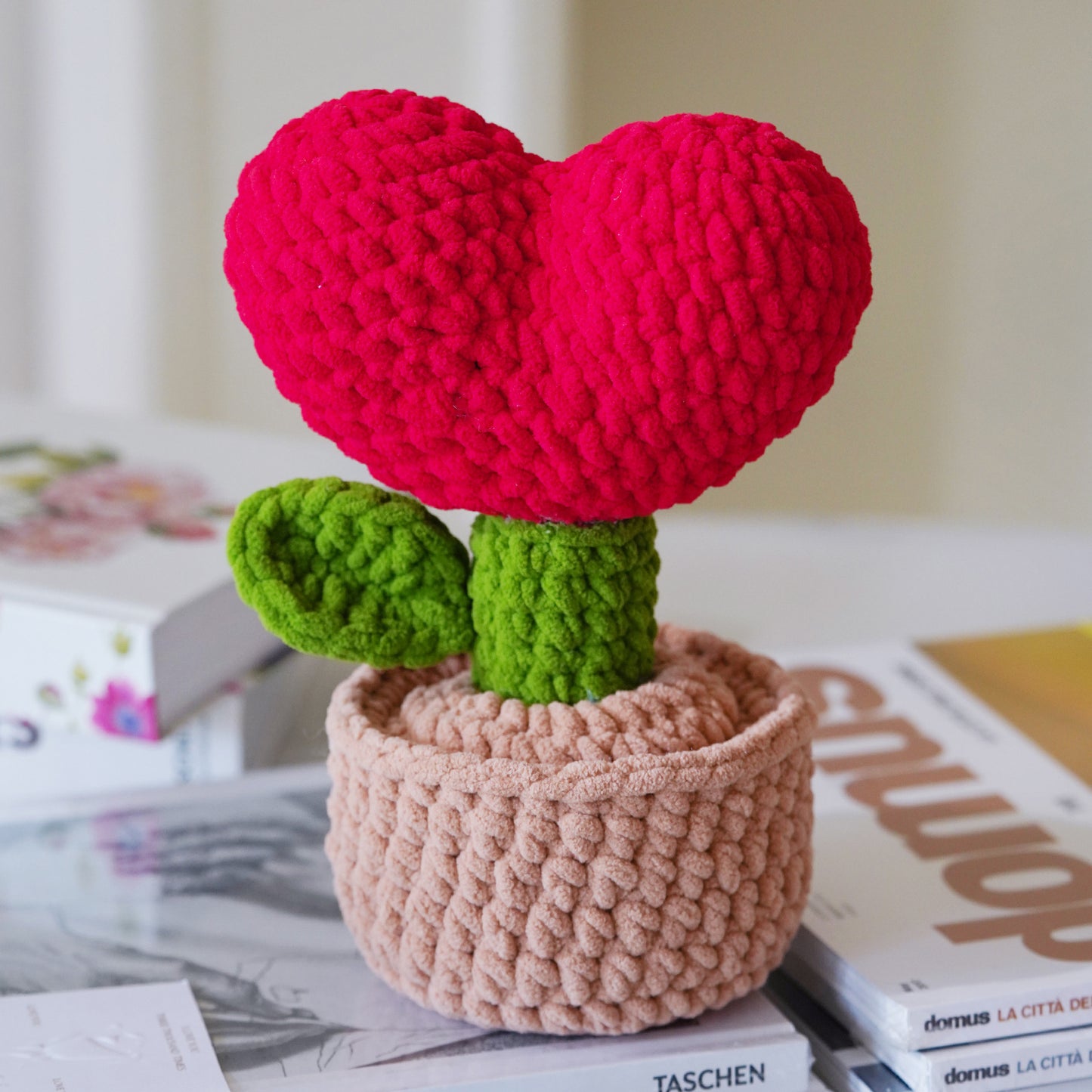 The Crochet Heart Plant Kit lets you make a heart-shaped plush on a green stem with leaves in a beige pot—perfect as charming DIY crochet home decor for your bookshelf or desk.