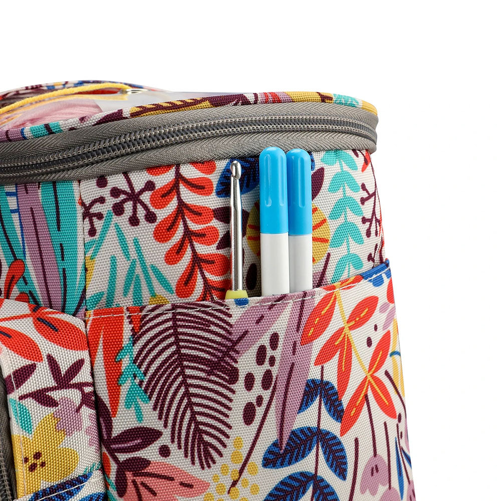 The Knitting Bag: Yarn Organizer, featuring a vibrant floral design and a gray zipper, contains two blue pens in its external pocket.