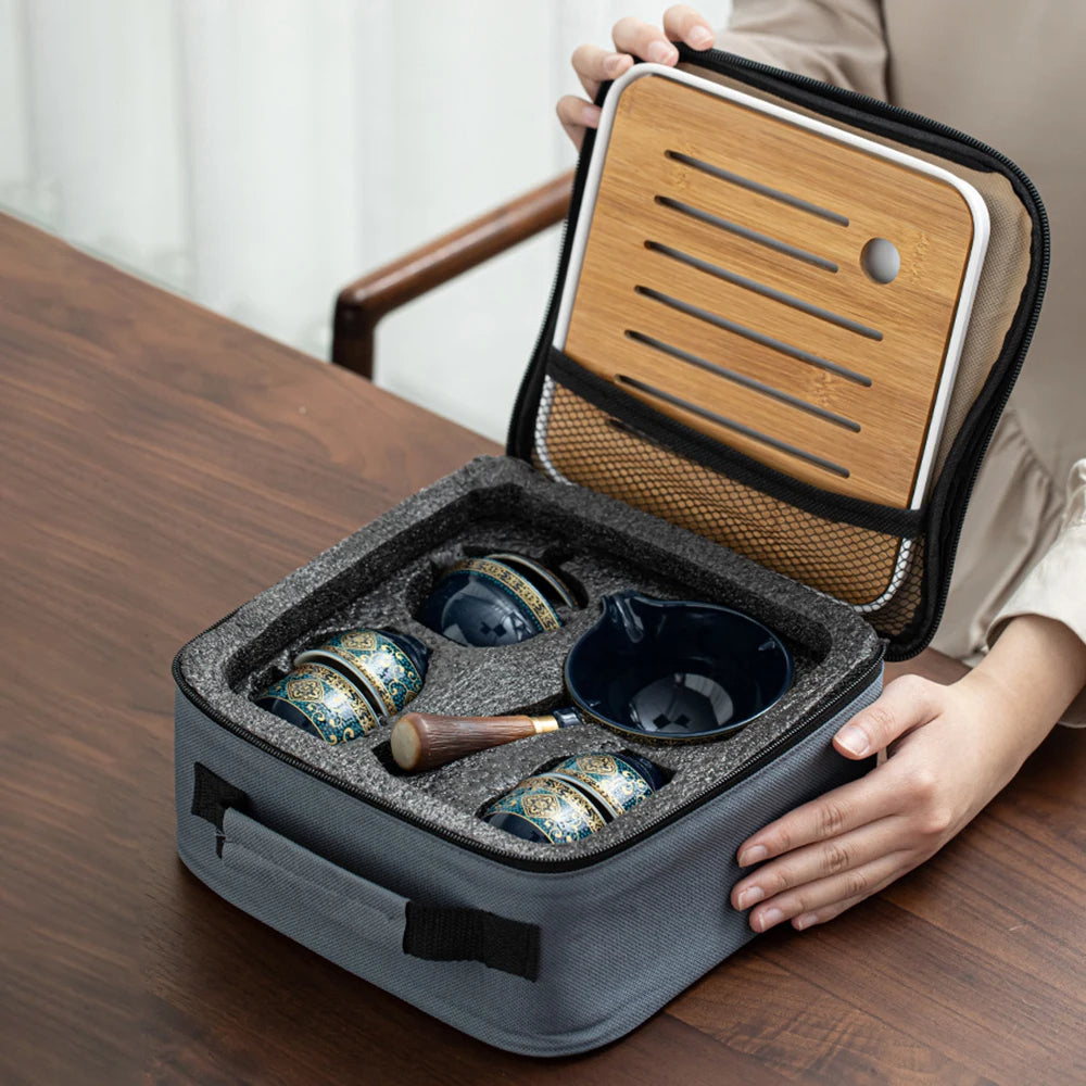 A person opens the gray carrying case, revealing the Tea Making Set With Cups and Case, which includes a porcelain tea maker, four decorative bowls, and a small mallet—ideal for any tea connoisseur.