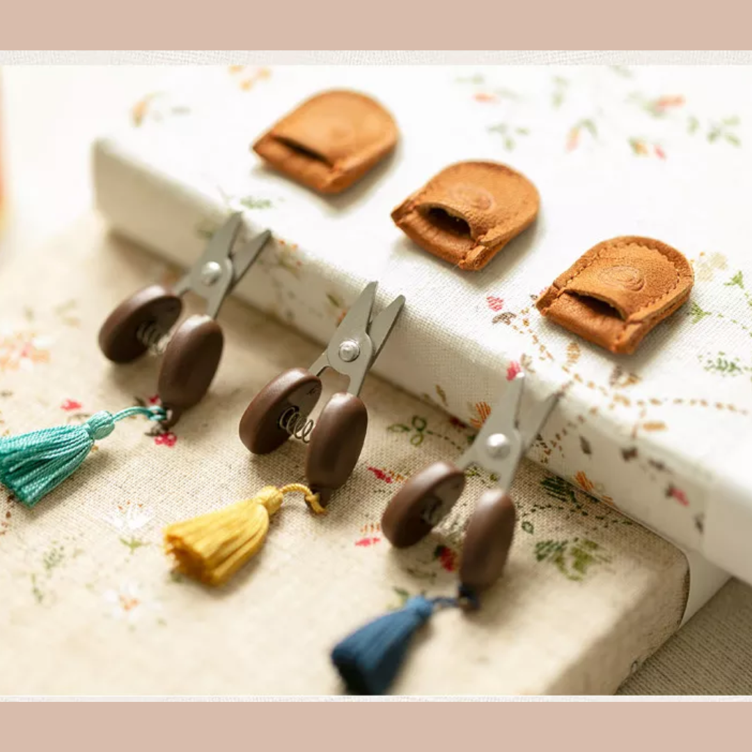 Compact and portable, the Small Scissors with leather covers and tassels are elegantly placed on a floral fabric background.