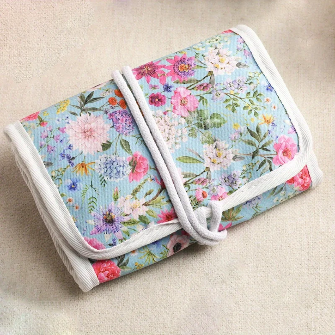 A stylish Crochet Hooks Organizer, featuring a floral-print fabric with white trim, lies on a beige surface, ideal for streamlined crafting.